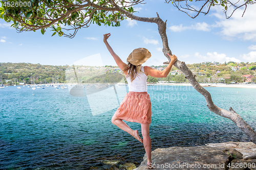 Image of Happy woman dance pirouette beside tree by the ocean