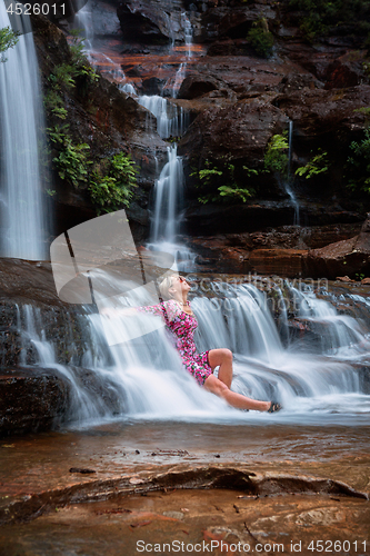 Image of Exhilaration in mountain waterfall, female sitting in flowing ca