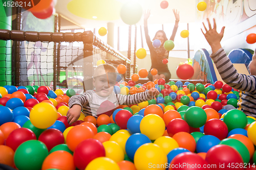 Image of young mom playing with kids in pool with colorful balls