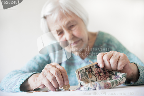 Image of Concerned elderly woman sitting at the table counting money in her wallet.