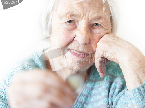 Image of Sad elderly woman sitting at the table at home and looking miserably at only remaining coin from pension in her hand.