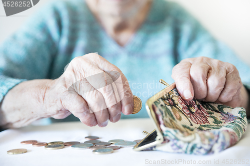 Image of Detailed closeup photo of unrecognizable elderly womans hands counting remaining coins from pension in her wallet after paying bills.