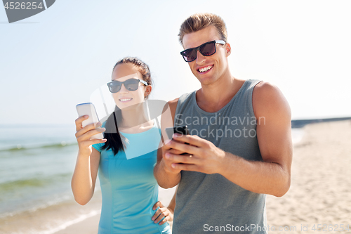 Image of couple in sports clothes with smartphones on beach