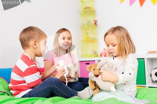 Image of happy children playing with soft toys at home