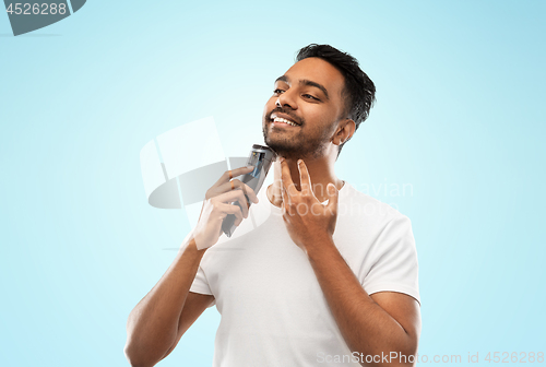 Image of smiling indian man shaving beard with trimmer