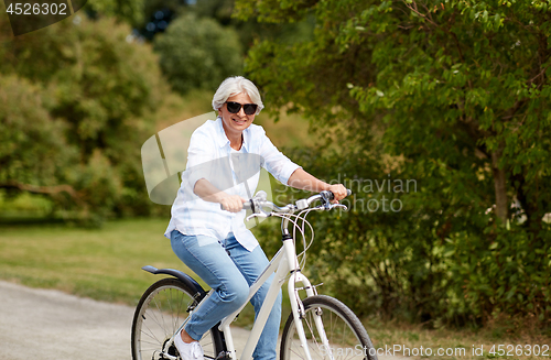 Image of happy senior woman riding bicycle at summer park