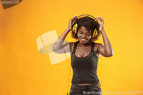 Image of Studio portrait of adorable curly girl happy smiling during photoshoot. Stunning african woman with light-brown skin relaxing in headphones