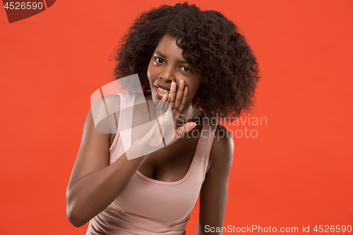 Image of The young woman whispering a secret behind her hand over red background
