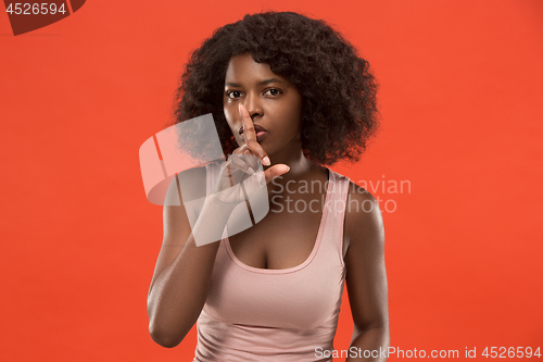 Image of The young woman whispering a secret behind her hand over red background
