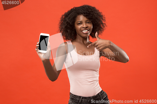 Image of Portrait of a confident casual afro girl showing blank screen mobile phone isolated over red background