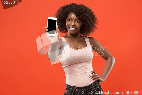 Image of Portrait of a confident casual afro girl showing blank screen mobile phone isolated over red background