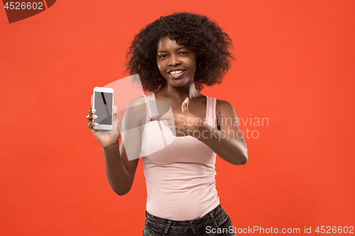 Image of Portrait of a confident casual afro girl showing blank screen mobile phone isolated over red background