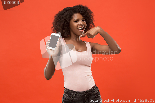 Image of Portrait of a confident casual afro girl showing blank screen mobile phone isolated over red background