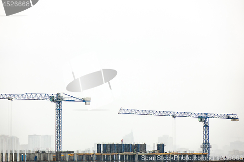 Image of Building under construction with two tower cranes against a gray cloudy sky.
