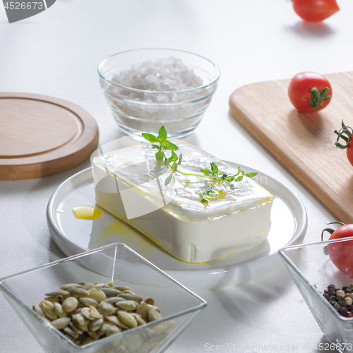 Image of In a white plate cheese with greens, peeled sunflower seeds and tomatoes on an unused kitchen table