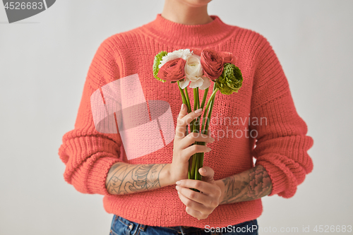 Image of A beautiful bouquet of flowers of a Ranunculus in a girl\'s hands with tatoo on a gray background. Trend color of the year 2019 Living Coral Pantone. Place for text.