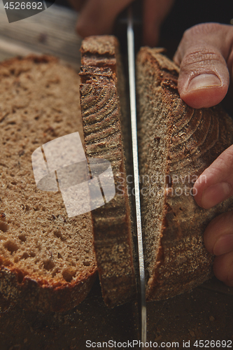 Image of young man\'s hand cut fresh dark bread