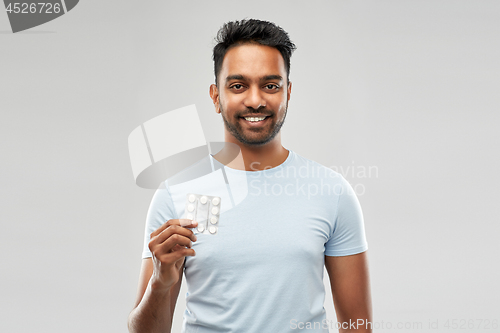 Image of smiling indian man with pills over grey background