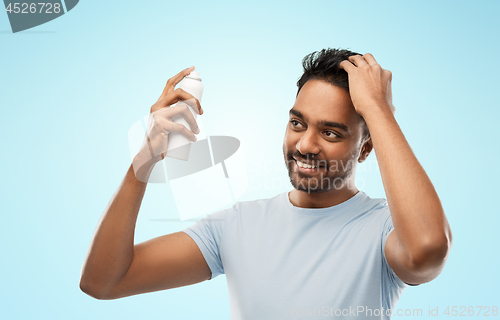 Image of smiling indian man applying hair spray over gray