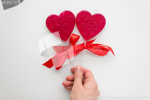 Image of close up of hand holding red heart shaped lollipop