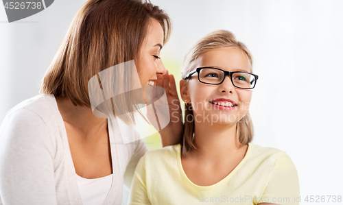 Image of happy mother whispering secret to daughter at home