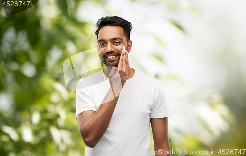 Image of happy indian man applying cream to face