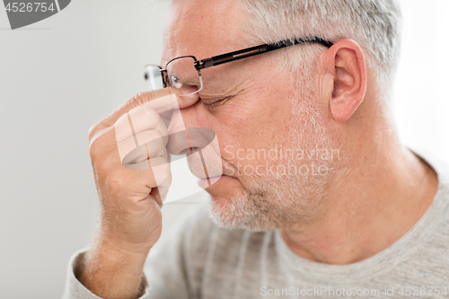 Image of senior man in glasses massaging nose bridge
