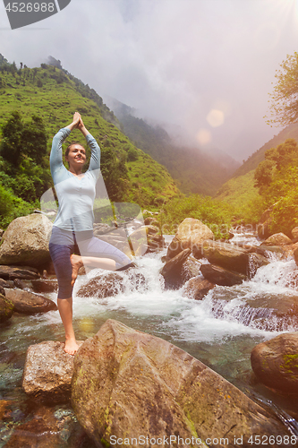 Image of Woman in yoga asana Vrikshasana tree pose at waterfall outdoors