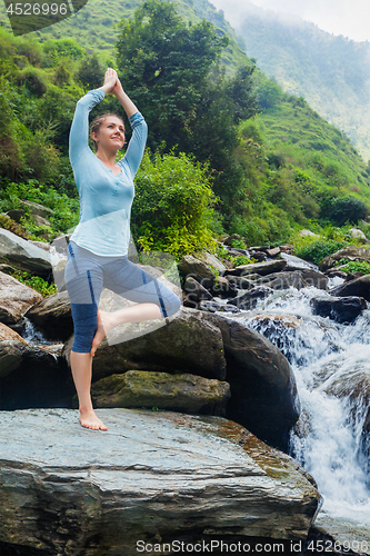 Image of Woman in yoga asana Vrikshasana tree pose at waterfall outdoors