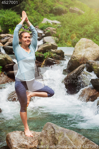 Image of Woman in yoga asana Vrikshasana tree pose at waterfall outdoors