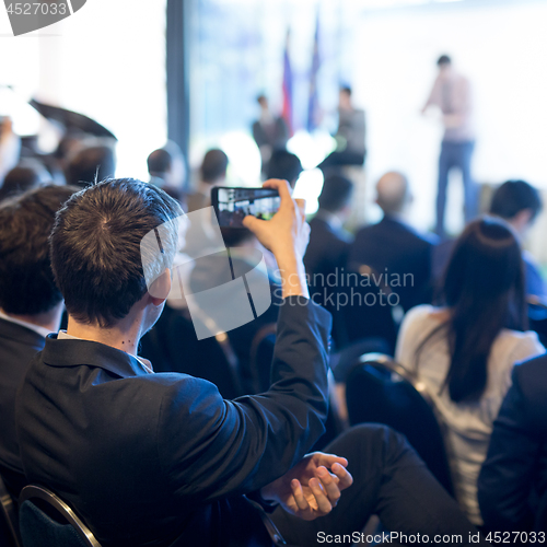 Image of Businessman takes a picture of corporate business presentation at conference hall using smartphone.