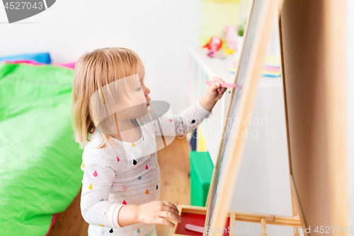 Image of happy little girl drawing on chalk board at home