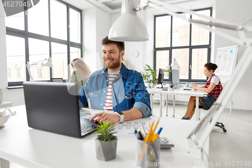 Image of smiling creative man with laptop working at office