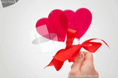 Image of close up of hand holding red heart shaped lollipop