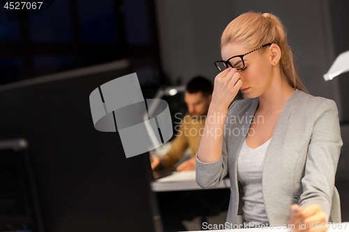 Image of businesswoman rubbing tired eyes at night office