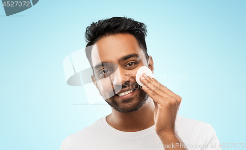 Image of smiling indian man cleaning face with cotton pad