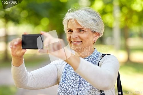 Image of senior woman photographing by cell at summer park