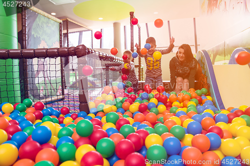 Image of young mom playing with kids in pool with colorful balls