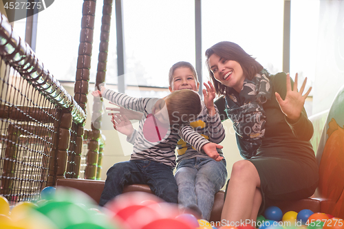 Image of young mom playing with kids in pool with colorful balls