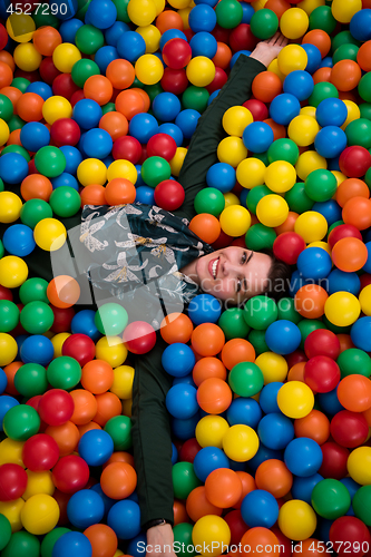 Image of young mom playing with kids in pool with colorful balls