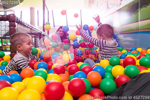 Image of young mom playing with kids in pool with colorful balls