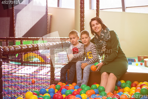 Image of young mom playing with kids in pool with colorful balls