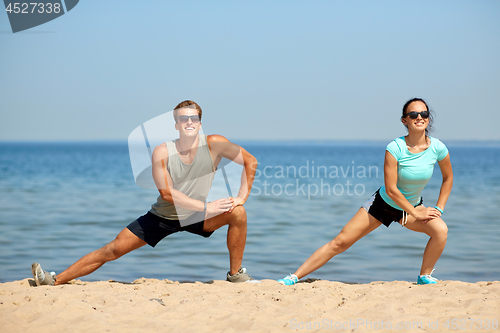 Image of smiling couple stretching legs on beach