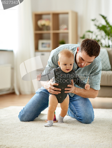 Image of father helping baby daughter with walking at home