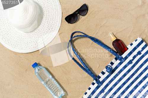 Image of beach bag, sunscreen, sunglasses and hat on sand