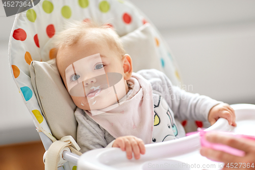 Image of little baby girl eating in highchair at home