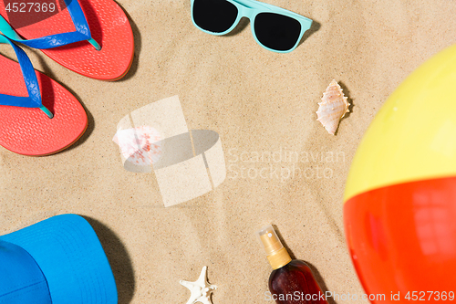 Image of cap, flip flops and shades and beach ball on sand