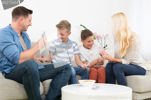 Image of Happy young family playing card game at home.