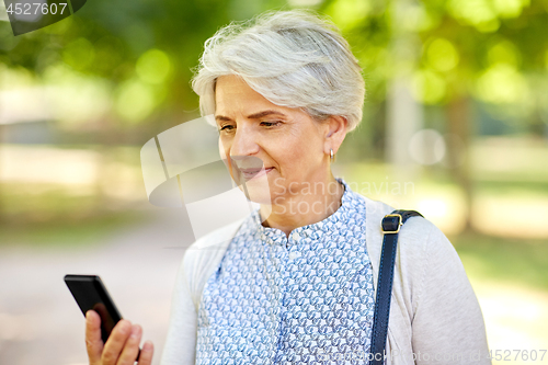 Image of happy senior woman with smartphone at summer park