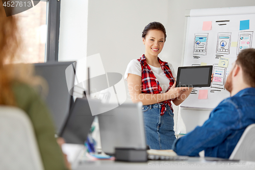 Image of woman showing tablet pc to creative team at office